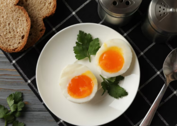 Ovos cozidos com gema mole, decorados com folhas de coentro, em um prato simples.