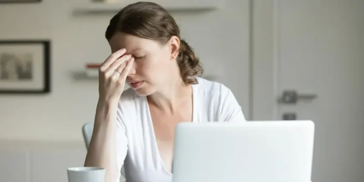 Mulher com expressão de cansaço e dor de cabeça, representando os efeitos do estresse no dia a dia.