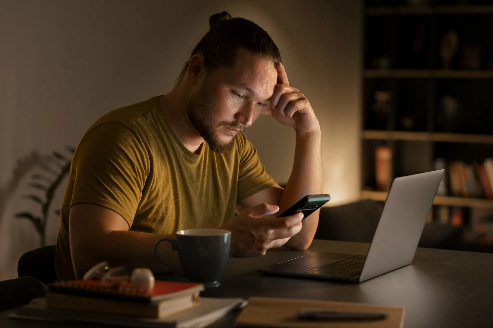 Pessoa usando celular e computador à noite, refletindo a dependência excessiva de dispositivos