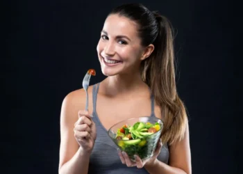 Mulher sorrindo enquanto segura uma tigela de salada fresca e um garfo com tomate cereja.