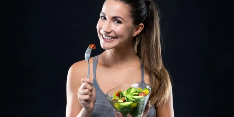 Mulher sorrindo enquanto segura uma tigela de salada fresca e um garfo com tomate cereja.