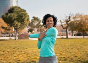 Mulher sorridente realizando exercício aeróbico em equipamento de remo, em ambiente de academia.