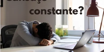 Homem sentado em uma mesa de trabalho com a cabeça apoiada nas mãos, mostrando sinais de cansaço constante.