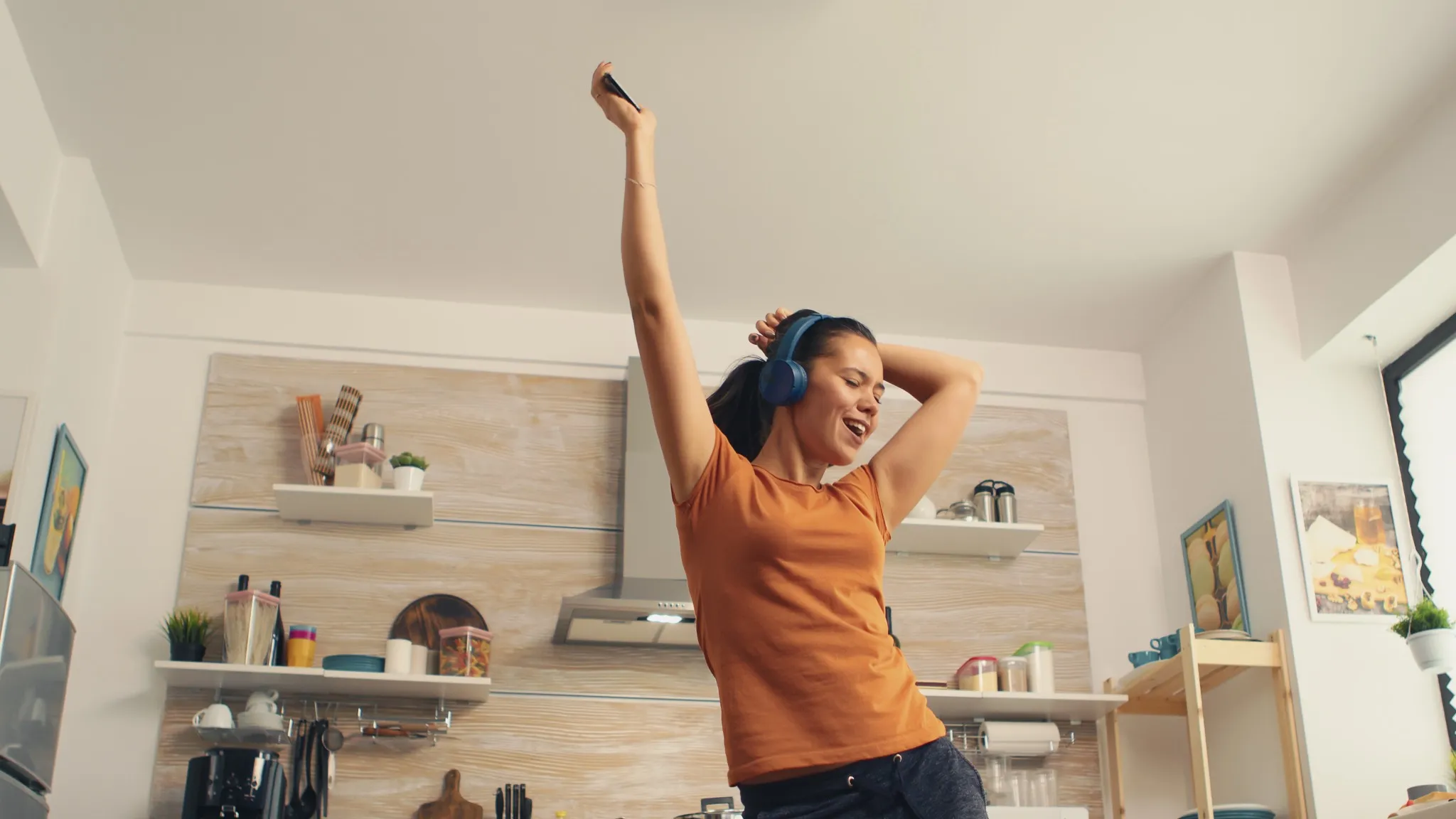 Mulher dançando na cozinha enquanto ouve música, ilustrando treino aeróbico com dança em casa.