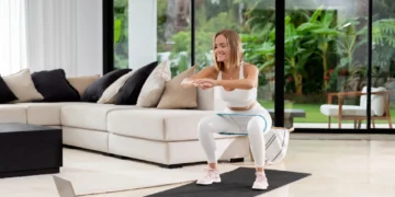 Mulher realizando agachamento em casa com elástico, durante treino eficaz.