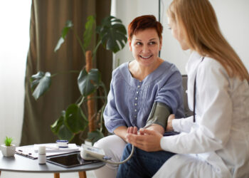 Paciente sorrindo enquanto médica mede sua pressão arterial em ambiente acolhedor.