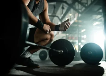 Homem se preparando para levantar barra com pesos em academia."