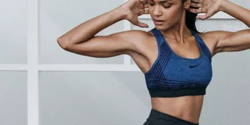 Mulher praticando exercício físico com foco na postura e definição muscular em ambiente de academia, usando top esportivo azul.