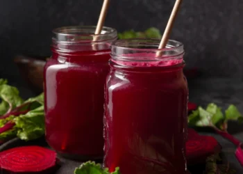 "Sucos de beterraba frescos em frascos de vidro com folhas de beterraba ao fundo."