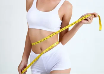 Mulher medindo sua cintura com uma fita métrica, simbolizando o processo de emagrecimento rápido e controle de peso.