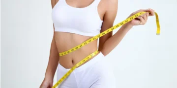 Mulher medindo sua cintura com uma fita métrica, simbolizando o processo de emagrecimento rápido e controle de peso.