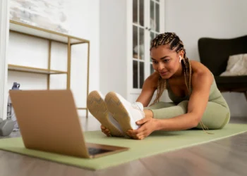 Mulher se alongando em casa enquanto segue uma rotina de treino com a ajuda de um laptop.