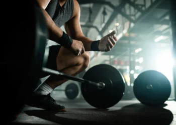 Atleta se preparando para levantar peso na academia, representando dedicação e disciplina nos exercícios.