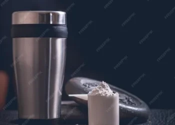 "Copo de metal para shake de proteína com uma medida de suplemento em pó."