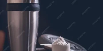 "Copo de metal para shake de proteína com uma medida de suplemento em pó."