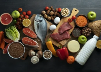Diversos alimentos saudáveis, incluindo frutas, vegetais, peixe, carne magra, grãos e laticínios, organizados em uma composição visual atraente.