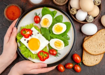 Prato com ovos cozidos e fritos, folhas verdes e tomate, representando uma refeição saudável e equilibrada.