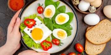 Prato com ovos cozidos e fritos, folhas verdes e tomate, representando uma refeição saudável e equilibrada.