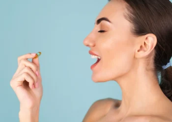 Mulher segurando uma cápsula de suplemento alimentar perto da boca, pronta para ingerir.