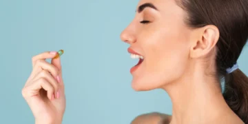 Mulher segurando uma cápsula de suplemento alimentar perto da boca, pronta para ingerir.