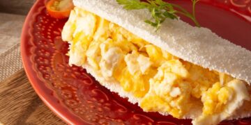 Tapioca recheada com ovos mexidos, servida em um prato vermelho