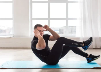 Homem fazendo abdominal remador em tapete azul durante treino funcional em ambiente iluminado.