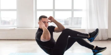 Homem fazendo abdominal remador em tapete azul durante treino funcional em ambiente iluminado.