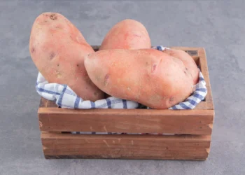 Batatas-doces frescas em uma cesta de madeira com um pano xadrez.