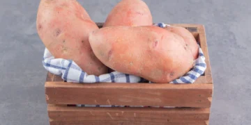 Batatas-doces frescas em uma cesta de madeira com um pano xadrez.