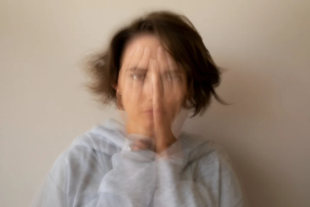 Imagem representando sintomas de ansiedade e desconforto, possivelmente associados à deficiência de vitamina B12, mostrando uma mulher com a mão no rosto, em um cenário borrado.