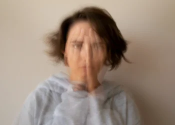 Imagem representando sintomas de ansiedade e desconforto, possivelmente associados à deficiência de vitamina B12, mostrando uma mulher com a mão no rosto, em um cenário borrado.