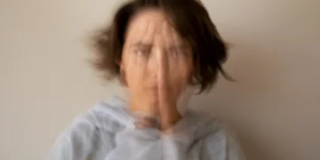 Imagem representando sintomas de ansiedade e desconforto, possivelmente associados à deficiência de vitamina B12, mostrando uma mulher com a mão no rosto, em um cenário borrado.