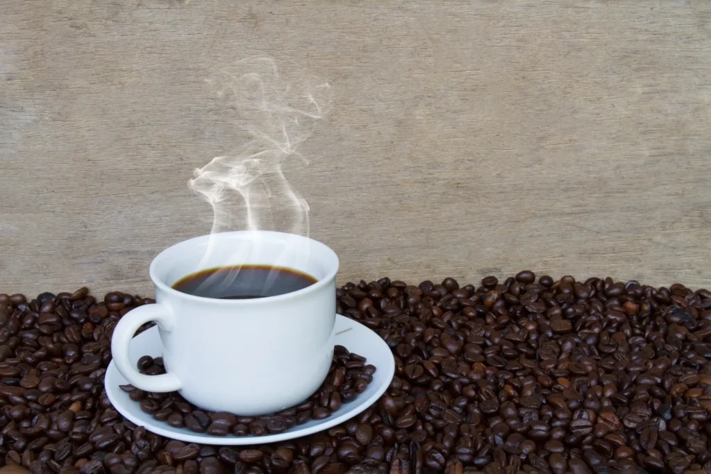 Xícara de café fumegante sobre grãos de café, simbolizando o aroma e o prazer do café fresco.