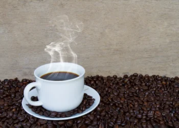 Xícara de café fumegante sobre grãos de café, simbolizando o aroma e o prazer do café fresco.