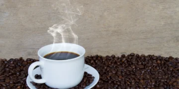 Xícara de café fumegante sobre grãos de café, simbolizando o aroma e o prazer do café fresco.