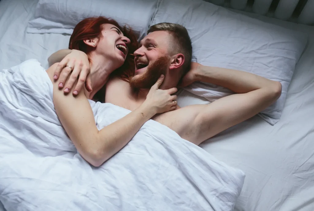 Casal sorrindo juntos na cama, demonstrando intimidade e conexão emocional