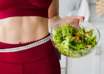 Mulher com fita métrica na cintura segurando uma tigela de salada, símbolo de dieta saudável