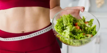 Mulher com fita métrica na cintura segurando uma tigela de salada, símbolo de dieta saudável