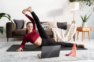 Mulher praticando exercícios físicos em casa, assistindo a uma aula online em seu laptop.
