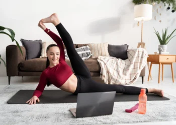 Mulher praticando exercícios físicos em casa, assistindo a uma aula online em seu laptop.