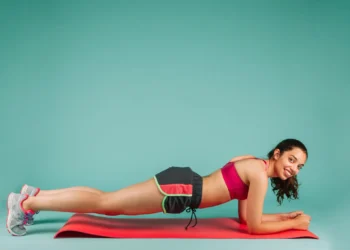 Mulher praticando exercícios físicos com um sorriso no rosto enquanto faz o exercício de prancha.