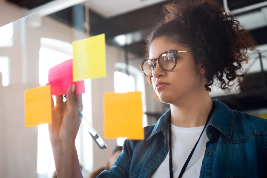 Mulher organizando ideias com post-its coloridos em painel de vidro.