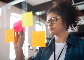 Mulher organizando ideias com post-its coloridos em painel de vidro.