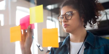 Mulher organizando ideias com post-its coloridos em painel de vidro.
