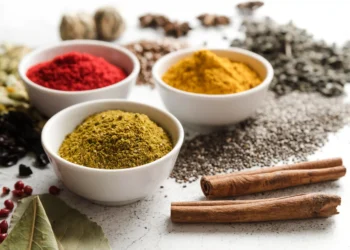 Diversos temperos e sementes orgânicas como pimenta, cúrcuma, canela e sementes sobre uma superfície clara.