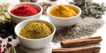 Diversos temperos e sementes orgânicas como pimenta, cúrcuma, canela e sementes sobre uma superfície clara.