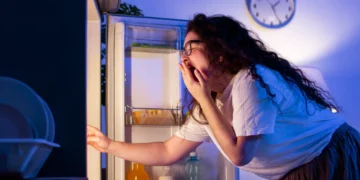 Mulher com sono abrindo a geladeira durante a madrugada em busca de algo para comer.