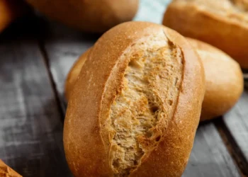 Pão francês fresco sobre tábua rústica de madeira, ilustrando dilemas alimentares