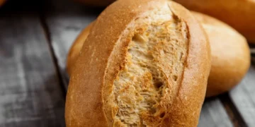 Pão francês fresco sobre tábua rústica de madeira, ilustrando dilemas alimentares