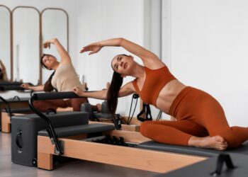 Mulher praticando Pilates no Reformer, realizando um exercício de alongamento,